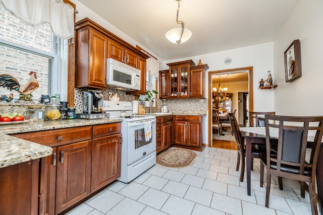 kitchen featuring white appliances, light stone countertops, sink, hanging light fixtures, and decorative backsplash