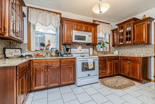 kitchen with backsplash, light stone counters, and white appliances