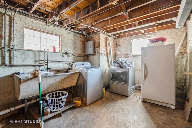 laundry area featuring electric panel, washer and dryer, a healthy amount of sunlight, and brick wall