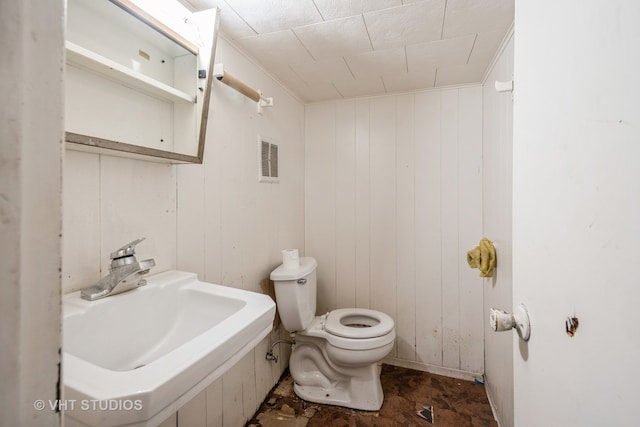 bathroom featuring wooden walls, toilet, and sink