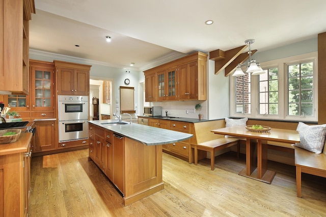 kitchen featuring a kitchen island with sink, hanging light fixtures, appliances with stainless steel finishes, breakfast area, and glass insert cabinets