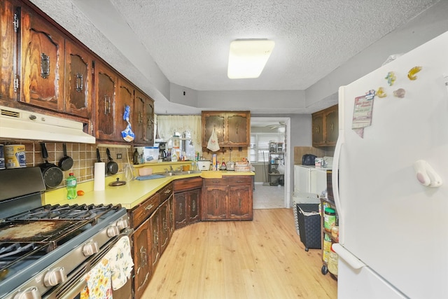 kitchen featuring tasteful backsplash, white refrigerator, a textured ceiling, stainless steel range with gas cooktop, and light hardwood / wood-style floors