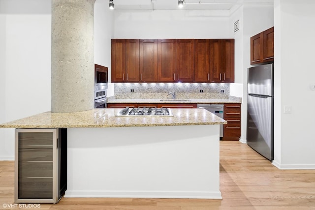 kitchen featuring light stone countertops, wine cooler, kitchen peninsula, appliances with stainless steel finishes, and light wood-type flooring