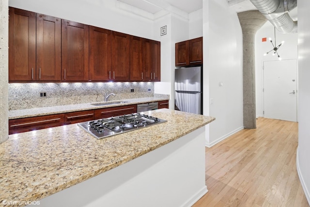 kitchen featuring backsplash, sink, light wood-type flooring, appliances with stainless steel finishes, and light stone counters