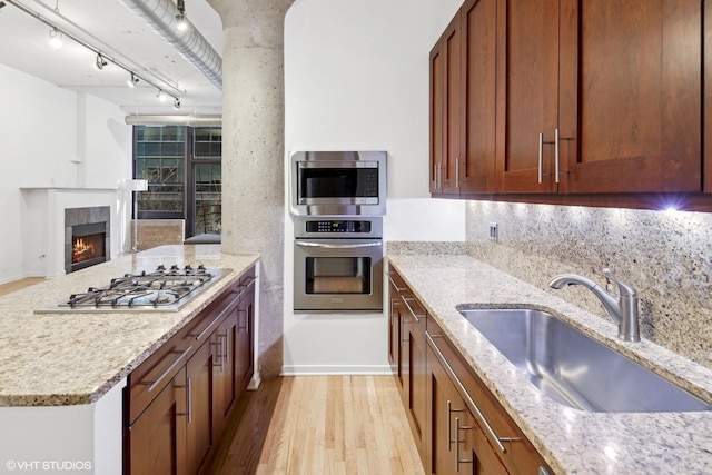 kitchen with appliances with stainless steel finishes, track lighting, light stone counters, sink, and light hardwood / wood-style floors