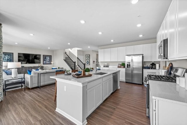 kitchen with sink, an island with sink, white cabinetry, stainless steel appliances, and dark hardwood / wood-style floors