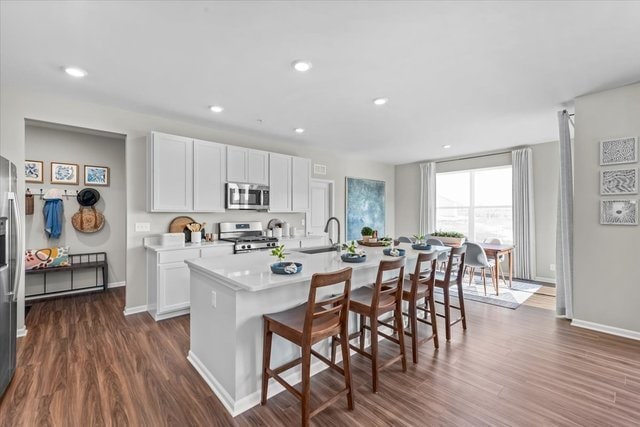 kitchen with dark wood-type flooring, appliances with stainless steel finishes, a kitchen island with sink, and white cabinetry