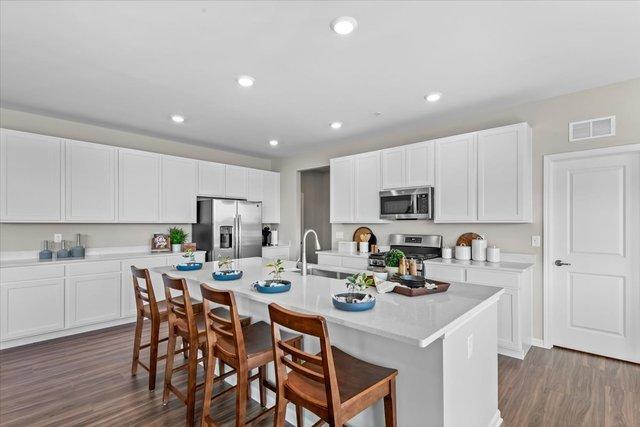 384 W Point Cir, Algonquin, IL 60102 - kitchen with appliances with stainless steel finishes, a sink, a breakfast bar area, dark wood-style flooring, and a center island with sink