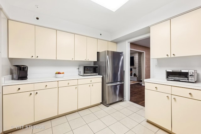 kitchen featuring stainless steel fridge, light tile patterned floors, and cream cabinets