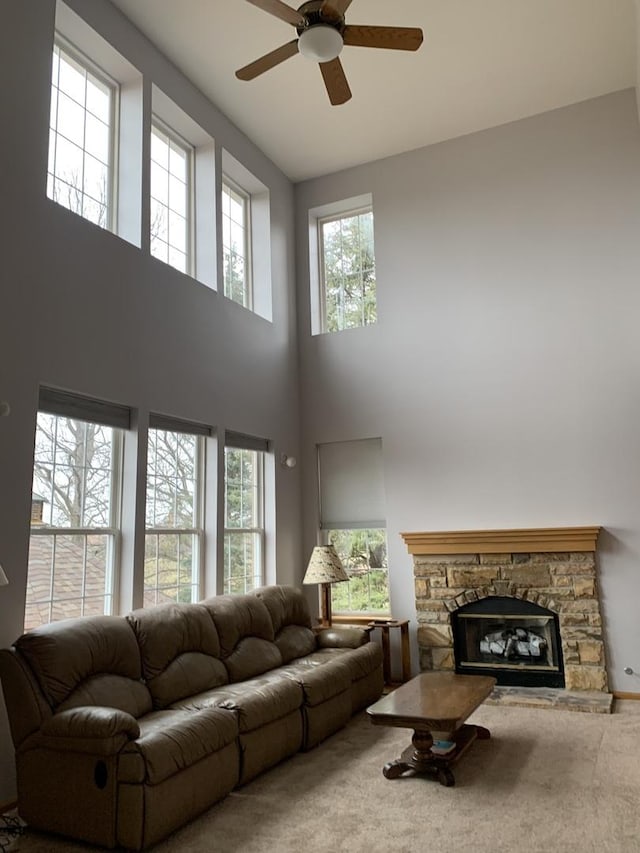 living room with carpet, ceiling fan, a fireplace, and a high ceiling