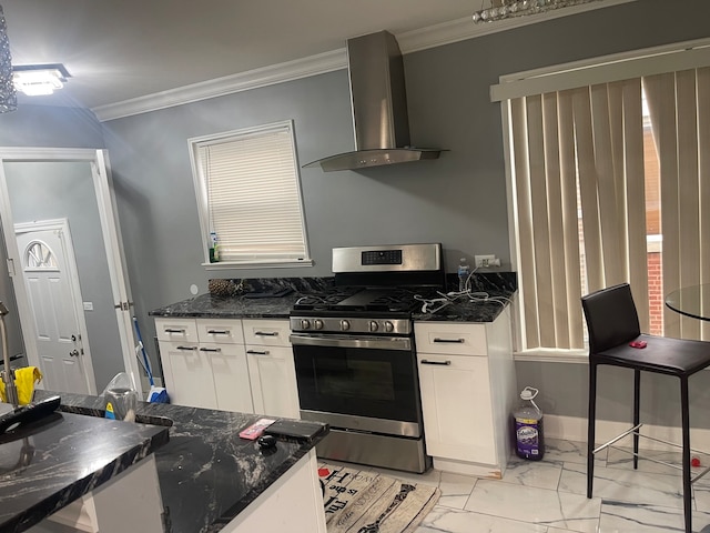 kitchen featuring wall chimney exhaust hood, ornamental molding, stainless steel gas range oven, white cabinetry, and dark stone countertops