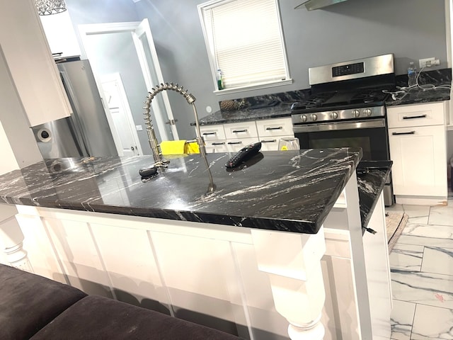 kitchen with white cabinetry, stainless steel appliances, a breakfast bar area, and dark stone countertops