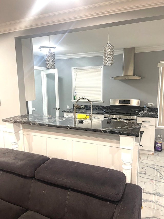 kitchen featuring wall chimney range hood, stainless steel gas range, pendant lighting, white cabinets, and dark stone countertops