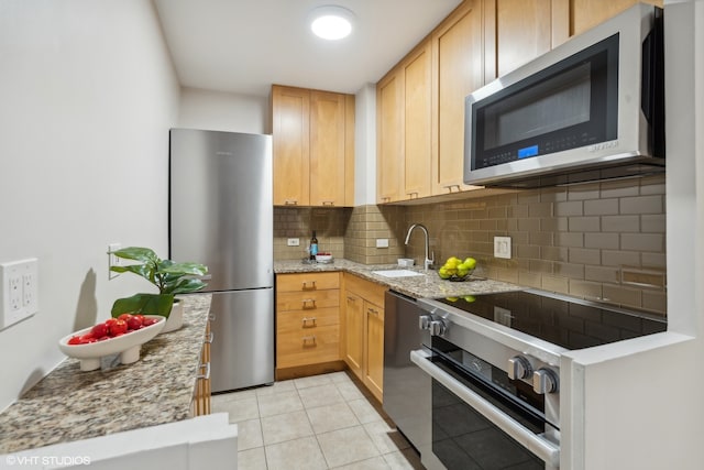 kitchen with decorative backsplash, light stone counters, light tile patterned floors, sink, and stainless steel appliances