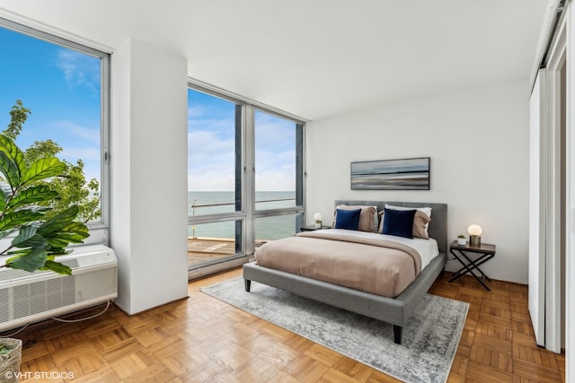 bedroom with light parquet floors, a water view, and an AC wall unit