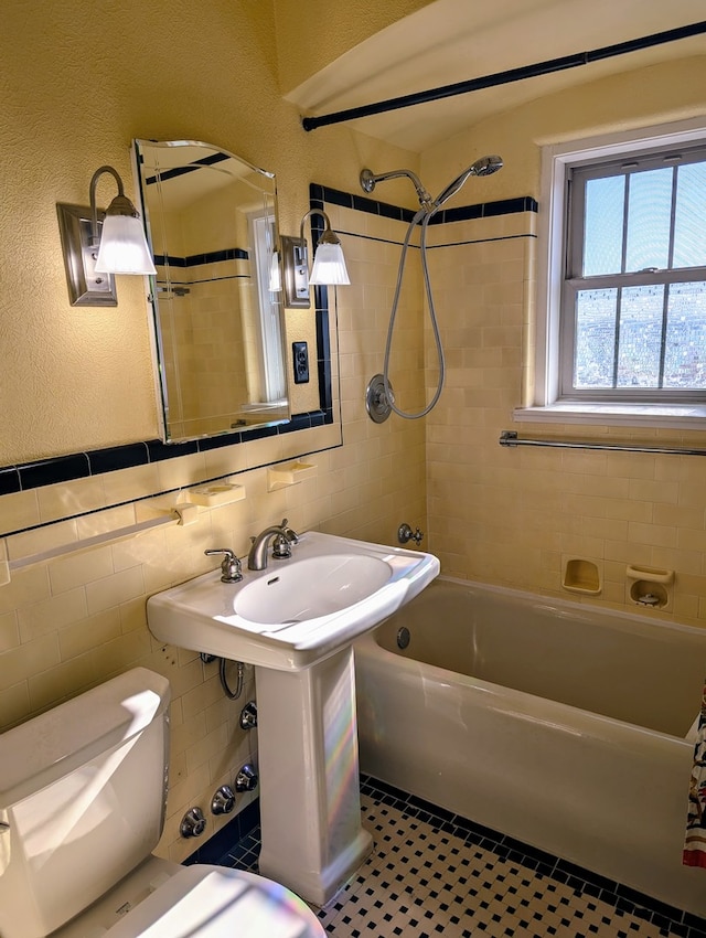 bathroom with tile patterned flooring, tiled shower / bath, toilet, and tile walls