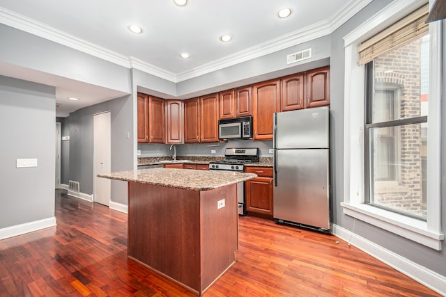 kitchen featuring stainless steel appliances, wood-type flooring, crown molding, and light stone counters