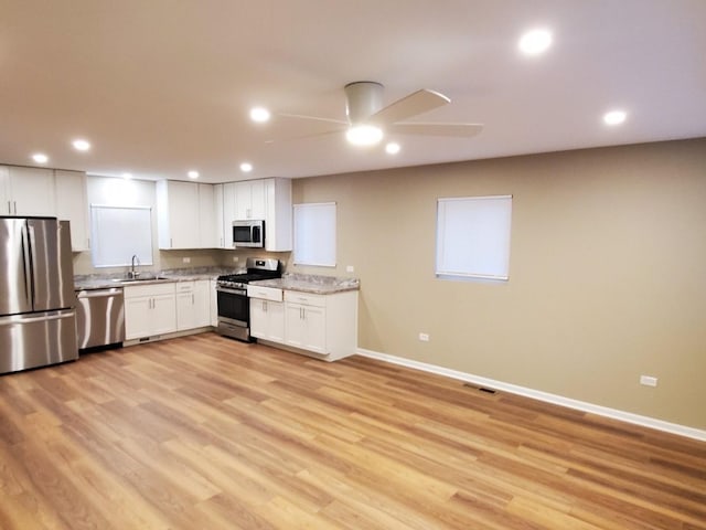 kitchen with sink, white cabinetry, light stone counters, appliances with stainless steel finishes, and light hardwood / wood-style floors