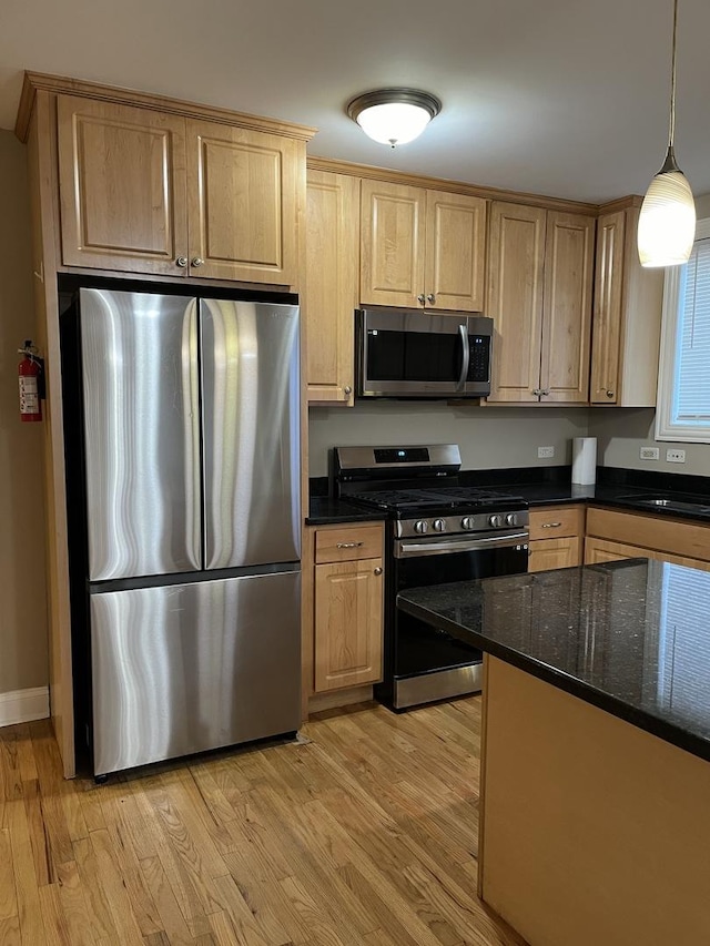 kitchen with pendant lighting, dark stone counters, sink, light hardwood / wood-style flooring, and appliances with stainless steel finishes