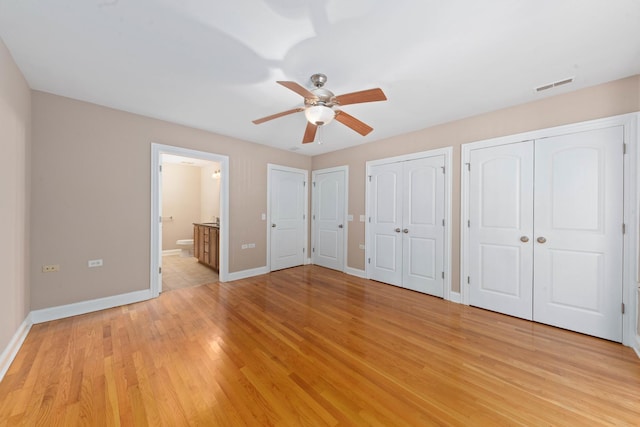 unfurnished bedroom featuring ceiling fan, light hardwood / wood-style floors, connected bathroom, and multiple closets