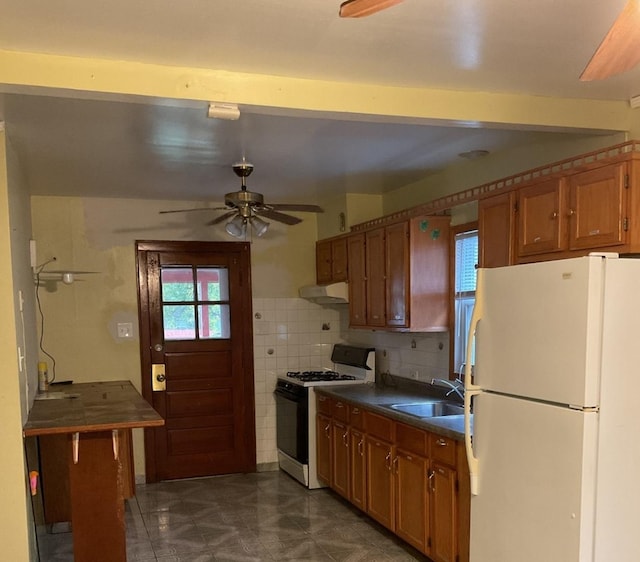 kitchen with a sink, freestanding refrigerator, under cabinet range hood, range with gas stovetop, and dark countertops