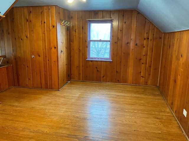 bonus room with wood walls, light wood-type flooring, and lofted ceiling