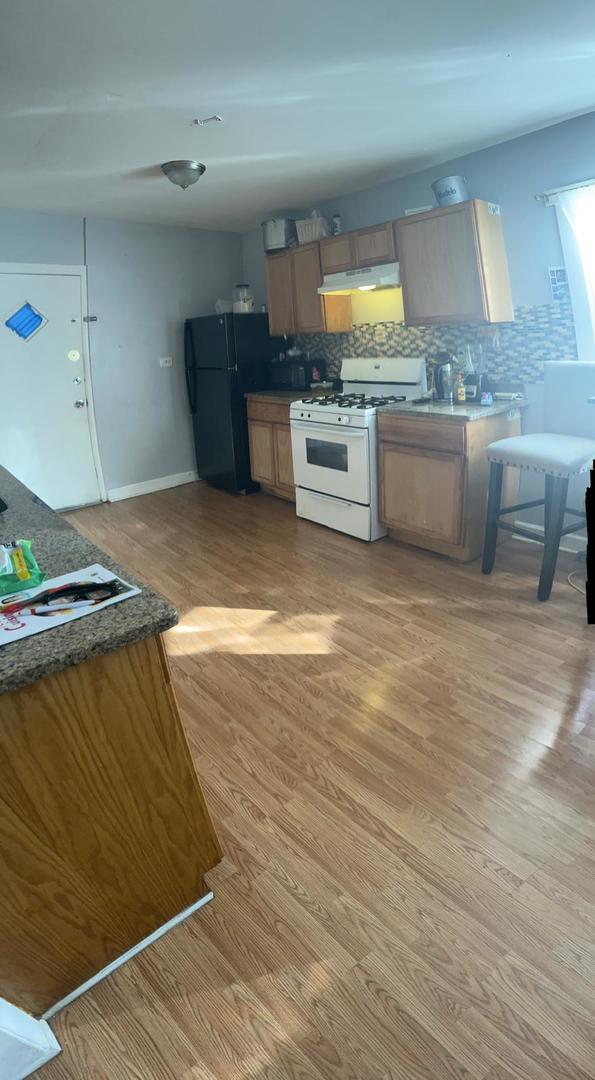 kitchen featuring white range with gas stovetop, backsplash, light hardwood / wood-style flooring, and black refrigerator