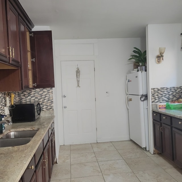 kitchen with light stone counters, sink, backsplash, and white fridge