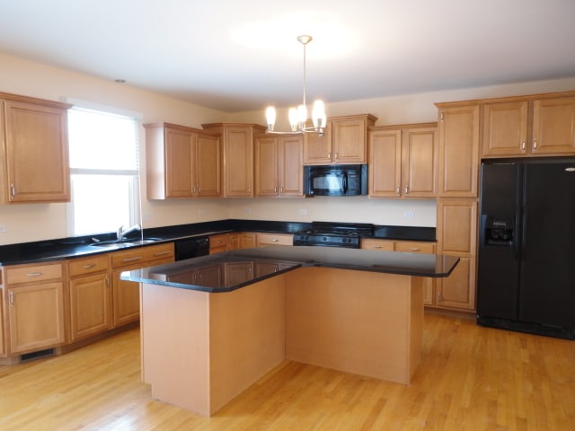 kitchen with black appliances, sink, a notable chandelier, a kitchen island, and light wood-type flooring