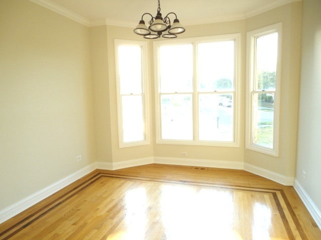 empty room with light wood-type flooring, crown molding, and an inviting chandelier