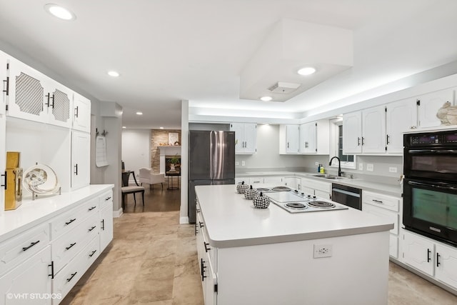 kitchen with stainless steel appliances, sink, white cabinetry, a kitchen island, and a stone fireplace