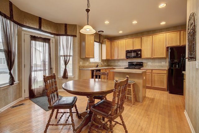 kitchen with black appliances, light wood-type flooring, light brown cabinetry, pendant lighting, and sink