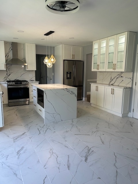 kitchen featuring stainless steel appliances, white cabinetry, light stone countertops, wall chimney exhaust hood, and decorative light fixtures