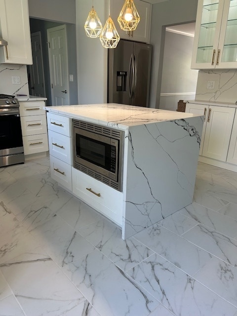 kitchen with white cabinetry, stainless steel appliances, hanging light fixtures, and light stone countertops