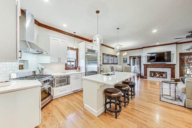 kitchen featuring sink, wall chimney range hood, built in appliances, pendant lighting, and white cabinets