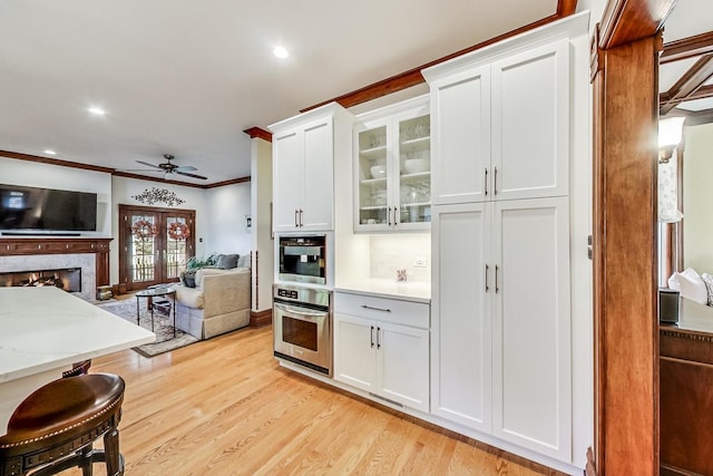 kitchen featuring light hardwood / wood-style flooring, white cabinetry, ornamental molding, and stainless steel oven