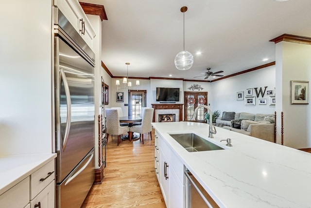 kitchen featuring white cabinetry, sink, built in refrigerator, light hardwood / wood-style floors, and decorative light fixtures