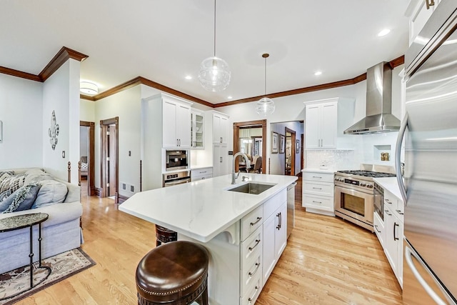 kitchen with wall chimney exhaust hood, premium appliances, sink, decorative light fixtures, and white cabinets