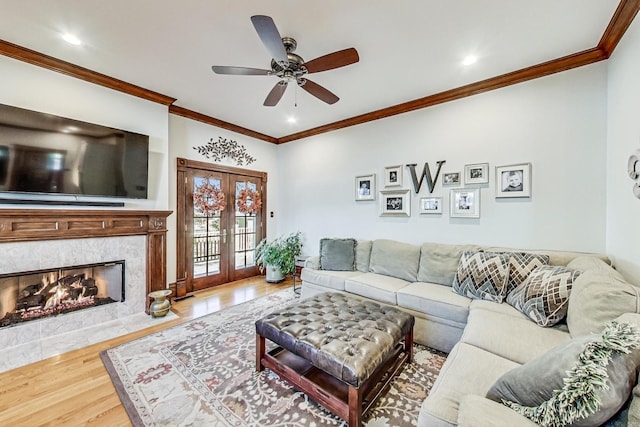 living room with a tiled fireplace, hardwood / wood-style floors, french doors, and ornamental molding