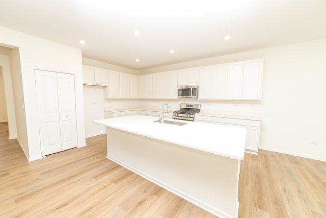 kitchen featuring stainless steel appliances, white cabinets, a kitchen island with sink, and light wood-type flooring