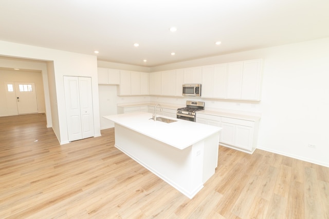 kitchen featuring stainless steel appliances, white cabinetry, sink, an island with sink, and light hardwood / wood-style floors