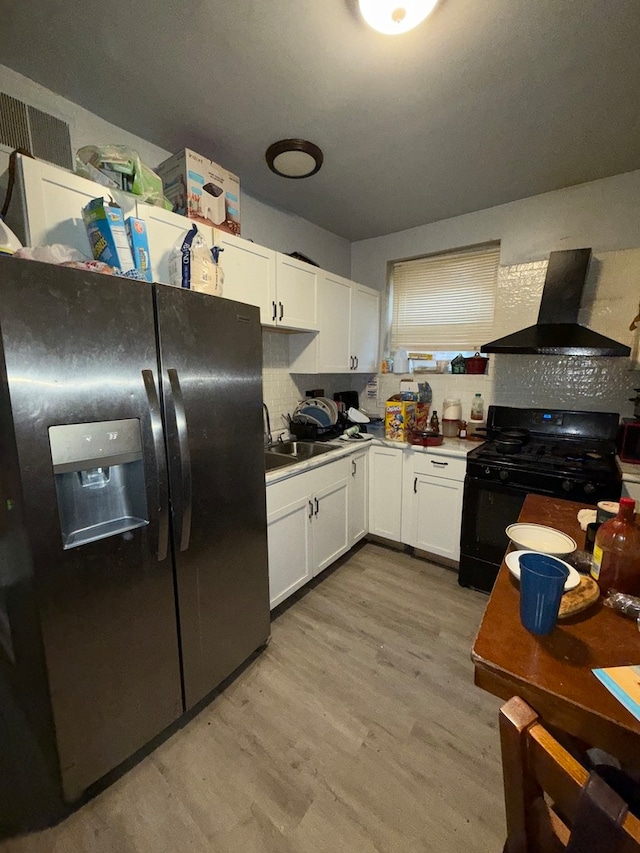 kitchen featuring black appliances, tasteful backsplash, white cabinets, wall chimney exhaust hood, and light hardwood / wood-style flooring