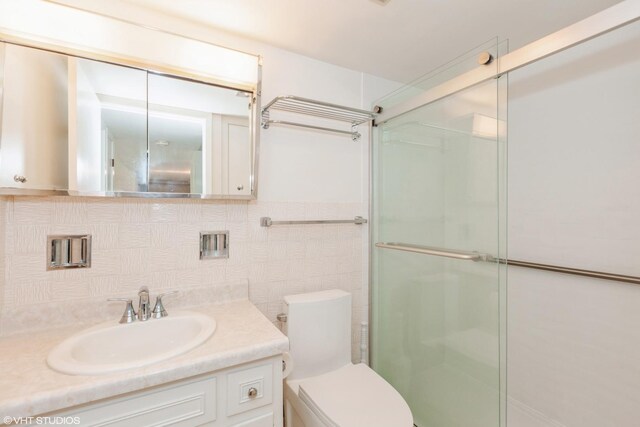 bathroom with vanity, tasteful backsplash, toilet, and an enclosed shower