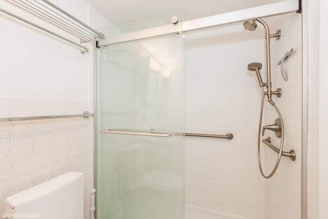 bathroom featuring a shower with door, tile walls, and toilet