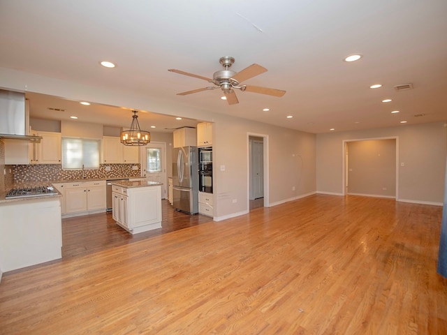 kitchen with stainless steel appliances, a center island, tasteful backsplash, pendant lighting, and light wood-type flooring