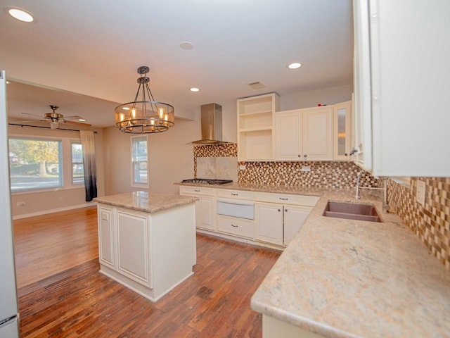 kitchen with light stone counters, hanging light fixtures, white cabinets, wall chimney exhaust hood, and a center island