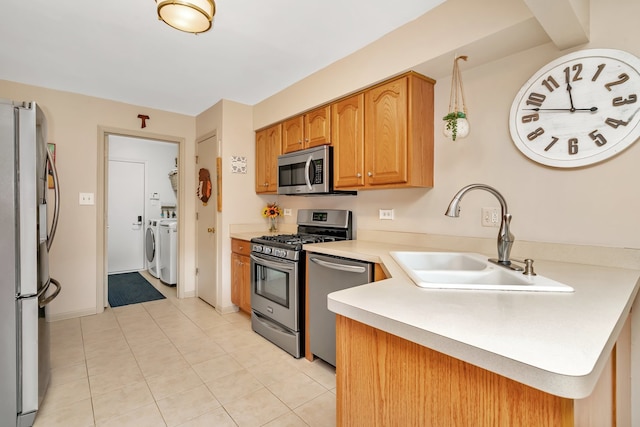 kitchen with sink, washer and dryer, light tile patterned floors, appliances with stainless steel finishes, and kitchen peninsula