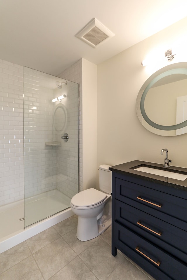 bathroom featuring tile patterned flooring, tiled shower, toilet, and vanity