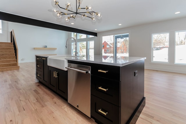 kitchen with dishwasher, sink, a kitchen island with sink, pendant lighting, and light wood-type flooring