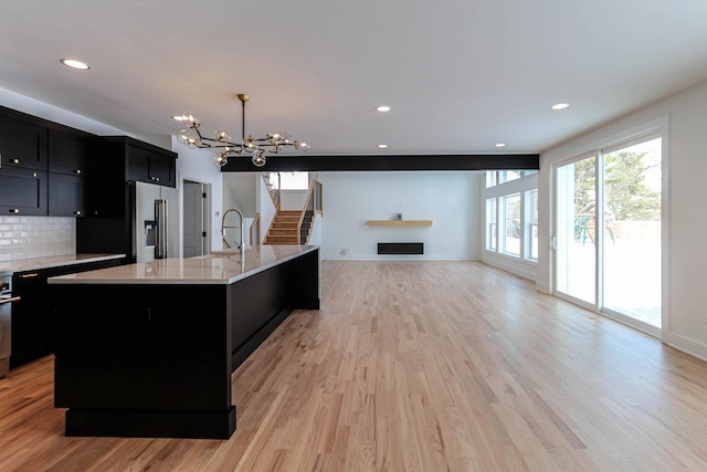 kitchen with light hardwood / wood-style flooring, hanging light fixtures, an island with sink, and high end refrigerator